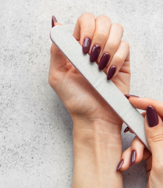 A person is carefully filing their nails at home, using a nail file to shape and smooth the edges, creating an elegant look for a manicure.